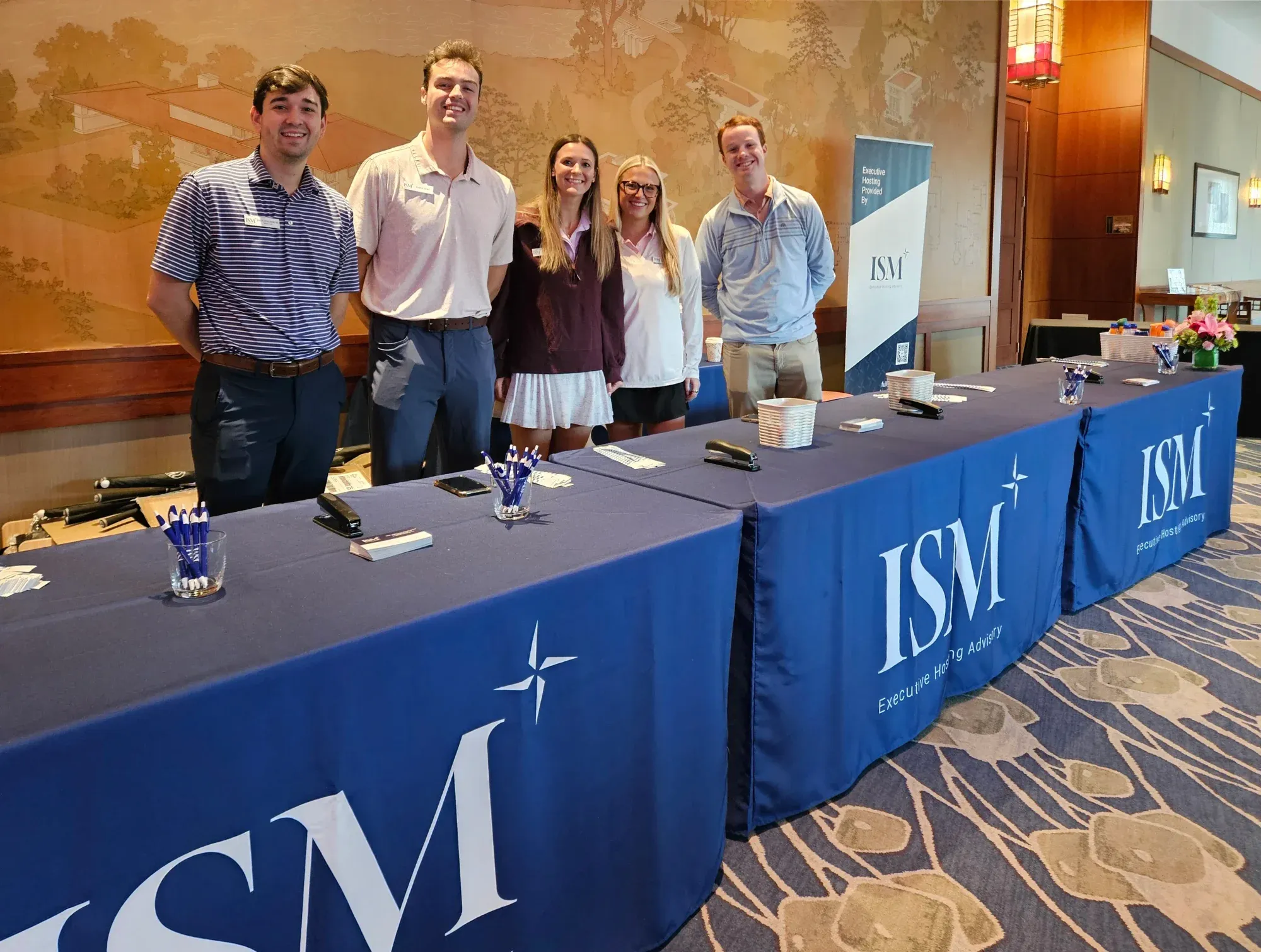 Five ISM team members stand behind ISM-branded registration tables.